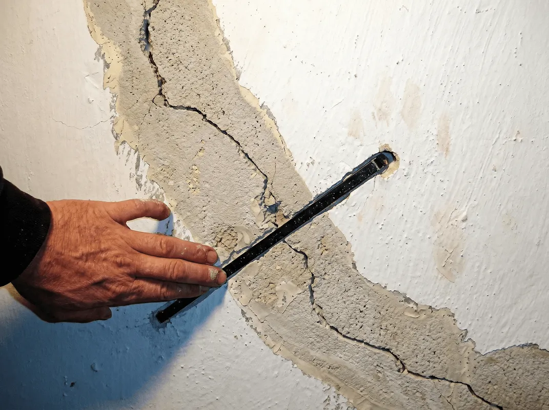 A wall with a large crack is being inspected by a professional in Dover, DE